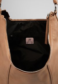 Sac à main beige avec fermeture éclair ouverte montrant la doublure intérieure noire et une poche intérieure zippée avec étiquette Anna Field.