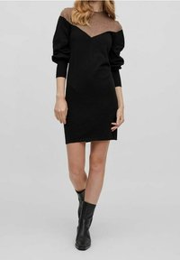 Schwarzes gestricktes Kleid mit einem kontrastierenden braunen Design an Schulter und Ärmeln. Mit V-Ausschnitt und gerippten Bündchen. Getragen mit schwarzen Ankle Boots.