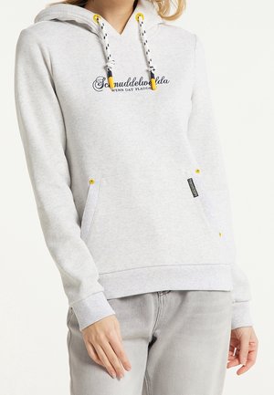Donna che indossa un felpa con cappuccio grigio chiaro con cordini neri e gialli e tasca frontale, abbinata a jeans grigi chiari.