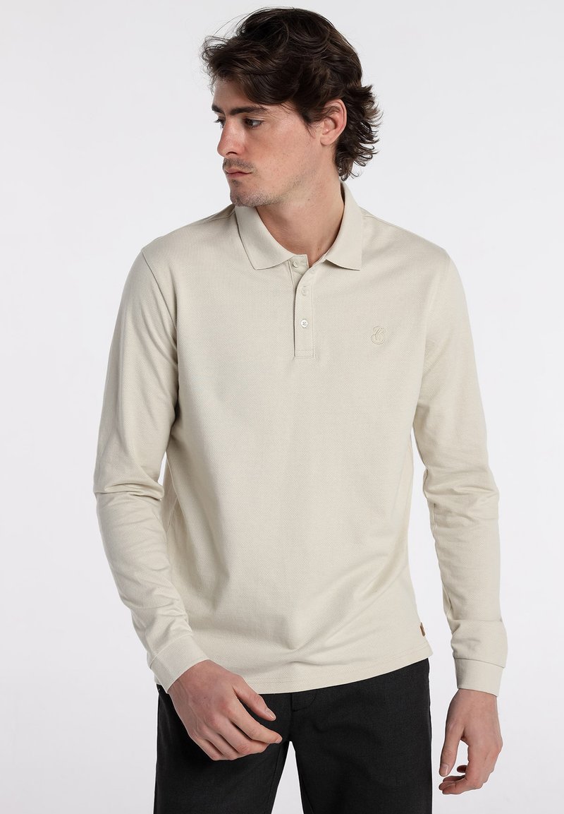 Langarm-Poloshirt in hellem Beige mit strukturierter Stoffqualität, Drei-Knopf-Leiste und dezentem Logodetail auf der Brust.