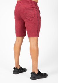 Rode sportieve shorts met een textuurpatroon, een elastische tailleband en een enkele achterzak. Gecombineerd met zwarte sportschoenen.