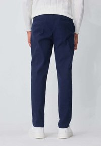 Pantalon bleu marine à coupe droite, doté de deux poches arrière et d'une texture lisse, associé à des sneakers blanches à profil bas.