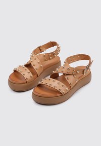 Sandalias de plataforma de ante con acentos de tachuelas, que presentan correas de cuero entrelazadas y una hebilla ajustable en el tobillo. Textura suave con punta redondeada.