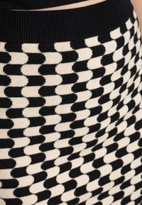 Jupe tricotée noire et crème présentant un motif géométrique avec des formes alternées, terminée par une taille côtelée noire unie.