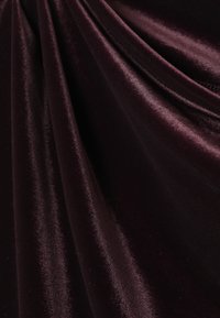 Dyb bordeauxvelourstof med en glat, skinnende overflade, der har bløde folder og en let glans. Ideel til elegant tøj eller polstring.