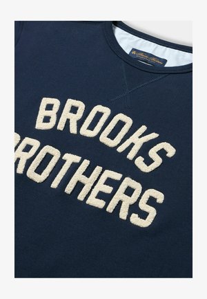 Felpa blu navy con lettering in crema "BROOKS BROTHERS" in rilievo. Visibili il colletto a coste e i dettagli di cucitura. Tessuto morbido al tatto.