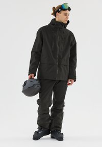 Schwarze wasserdichte Skijacke und -hose mit Reißverschlusstaschen, verstellbarem Kapuze und schlankem Design, kombiniert mit einem grauen Helm.