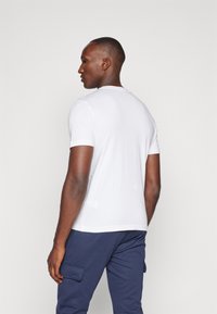 White short-sleeve t-shirt made of cotton, featuring a round neckline and a relaxed fit, worn with navy cargo pants.