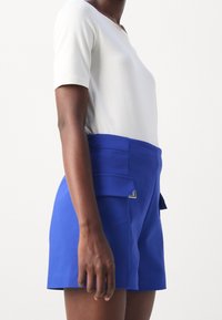 Blue high-waisted shorts with a sleek design, made of smooth fabric. Features front pockets and a silver hardware accent.