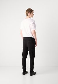 Schwarze Cargo-Hosen mit Seitentaschen und elastischen Bündchen, kombiniert mit einem schlichten weißen T-Shirt. Das Outfit wird durch schwarze Sneakers abgerundet.