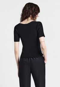 Top in maglia a coste nera con maniche corte, caratterizzato da un colletto rotondo e un orlo leggermente curvato, abbinato a pantaloni neri su misura.