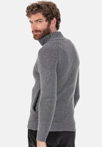 Pull gris en maille avec un col montant et des poches latérales, présentant un tissu texturé ainsi que des poignets et un ourlet c ôtelés.