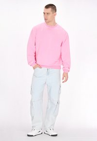 Felpa rosa chiaro con maniche lunghe e polsini a costine, abbinata a pantaloni cargo blu chiaro con tasche laterali e vestibilità rilassata.