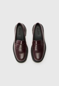 Bordeaux lær loafers med rund tå, polstret krave og kontrastfarget svart gummisåle. Har dekorativ søm og logo på sålen.