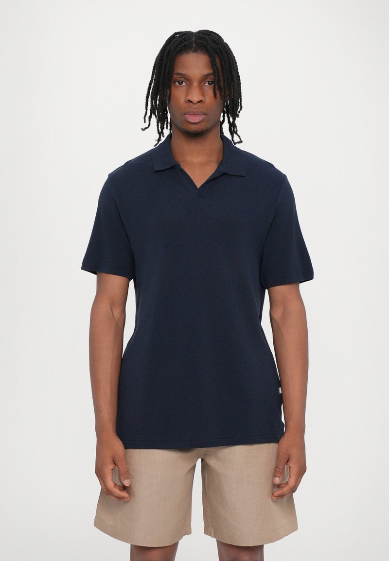 Polo de color azul marino con una textura suave, de manga corta y con un cuello con muesca, combinado con pantalones cortos beige para un look casual.