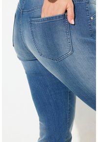 Farkut keskisinisessä pesussa, joissa on kapea malli. Ominaisuuksiin kuuluu takatasku ja ommellut yksityiskohdat, jotka korostavat sileää pintaa.