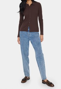 Brown ribbed long-sleeve shirt with pointed collar, button front, paired with light blue high-waisted jeans and brown loafers.