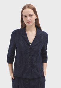 Námornícky modrý štruktúrovaný blazer s vertikálnymi prúžkami, s klopovým golierom, trojštvrťovými rukávmi a dvoma prednými gombíkmi. Obsahuje jeden vrecko na hrudi.