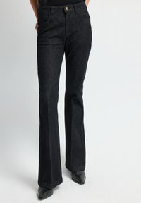 Zwarte flared jeans van denim met een strakke taille, vier zakken en gouden knoopdetails. Soepele textuur met lichte stretch voor comfort.