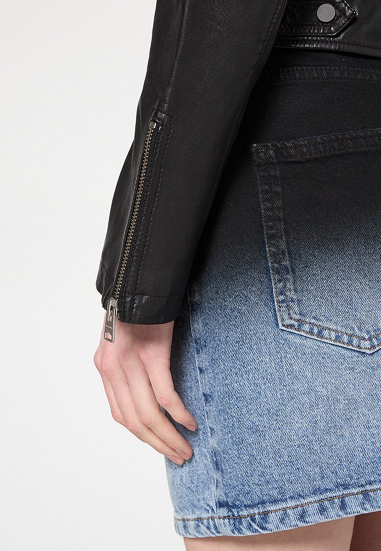 Giacca in pelle nera con polsini con zip e una gonna di jeans che presenta una sfumatura ombre dal blu scuro al blu chiaro, enfatizzando la texture e i dettagli.