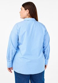 Camicia a righe azzurra chiara con maniche lunghe, colletto strutturato e polsini con bottone. Il tessuto appare liscio con una vestibilità comoda.
