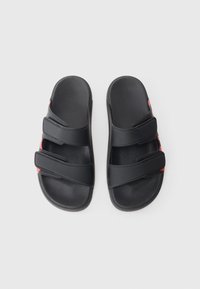 Saboti negri din plastic texturat, cu trei curele reglabile cu velcro și accente roșii. Talpă plată, design minimalist.
