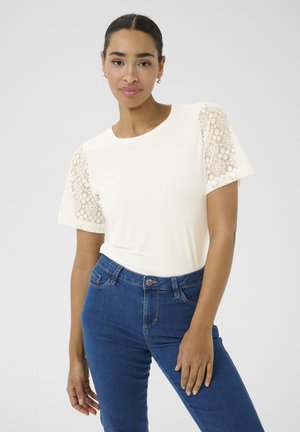 Creme T-shirt med blonde korte ærmer, parret med mørkeblå jeans; glat stof og tætsiddende design med rund halsudskæring.