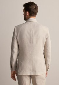 Veste de costume en lin beige clair avec une fente simple, coupe ajustée et texture subtile ; dispose de trois boutons sur les manches et de revers crantés.