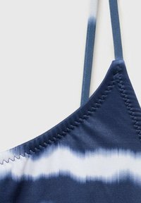 Bikini top v barvah mornarice in bele, z regulatorjem, gladko teksturo in cik-cak šivom vzdolž ovratnika.