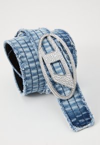 Jeansbelte med teksturert, frynsete kant og en sølvfarget oval spenne prydet med rhinestones, som gir en dekorativ kontrast.