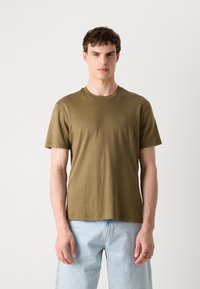 Olivenfarget bomull T-skjorte med rund hals, korte ermer og en diskret logo på brystet, kombinert med lyseblå jeans.