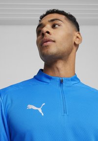 Blaues Viertelzip-Sportoberteil mit strukturiertem Finish und weißem Puma-Logo auf der Brust. Verfügt über einen Stehkragen und kontrastierende Reißverschlussdetails.
