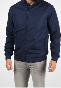 Navy blue bomber jacket with a zip front, ribbed cuffs, and hem. Features side pockets and smooth, lightweight fabric texture.
