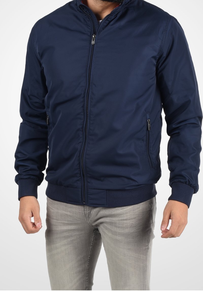 Navy blue bomber jacket with a zip front, ribbed cuffs, and hem. Features side pockets and smooth, lightweight fabric texture.