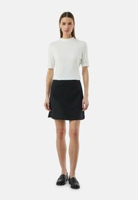 Witte geribde top met korte mouwen, gecombineerd met een zwarte A-lijn rok. Zwarte instappers maken de outfit compleet en tonen een minimalistisch ontwerp.