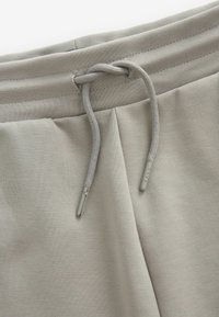 Los pantalones de chándal gris claro cuentan con una cintura con cordón ajustable con puntas plateadas, una cinturilla acanalada y una tela suave y texturizada.