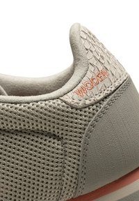 Beiger Sneakerabsatz mit Mesh-Gewebe, strukturiertem Einsatz und in Orange gesticktem "WOAKY", ausgestattet mit gepolstertem Kragen und genähten Details.