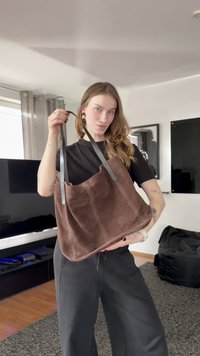 Brun semsket skinn shopper-veske med grå håndtak, som har en myk tekstur og et enkelt, uutsmykket design. Vesken holdes mot en lys bakgrunn.
