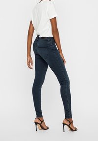 Slim-fit mörk denimjeans med hög midja, två bakfickor och diskreta sömnadsdetaljer, kombinerade med en vit t-shirt med rund hals och klackar.