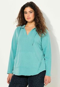 Turkoosi huppari, jossa on V-pääntie, etutasku ja ommellut yksityiskohdat. Ominaisuuksiin kuuluu rento istuvuus ja revityt helmaviimeistelyt.