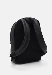 Zaino nero con un'esterno sintetico testurizzato, pannelli in rete, spallacci regolabili e una maniglia superiore per il trasporto.