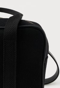 Κοντινός πλάνο γωνίας μαύρης υφασμάτινης τσάντας με υφασμένο λουρί και λεία λεπτομέρεια περιθωρίου σε απλό φωτεινό φόντο.