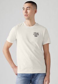 Tricou alb din bumbac cu mâneci scurte, având un text grafic imprimat în negru "HOUSE PLANTS" și "Levi's" în zona stângă a pieptului.