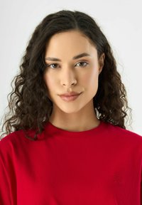 Rotes Baumwoll-T-Shirt mit Rundhalsausschnitt und kurzen Ärmeln, mit dezenten gestickten Blumenmotiven auf der Brust. Glatte Textur.