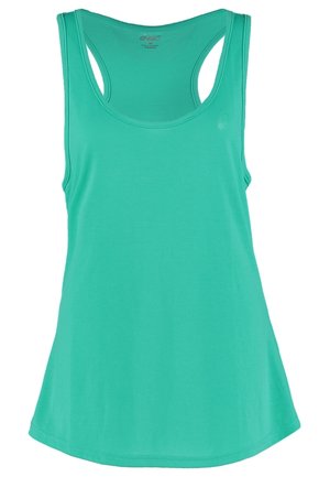 Femme debout portant un débardeur turquoise, un soutien-gorge de sport noir, des leggings noirs à motifs et des chaussures de sport noires sur fond clair.