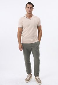 Beige strikket polo skjorte med V-hals, stribede detaljer på ærmerne, parret med lysegrønne bukser og beige sneakers. Enkel design.