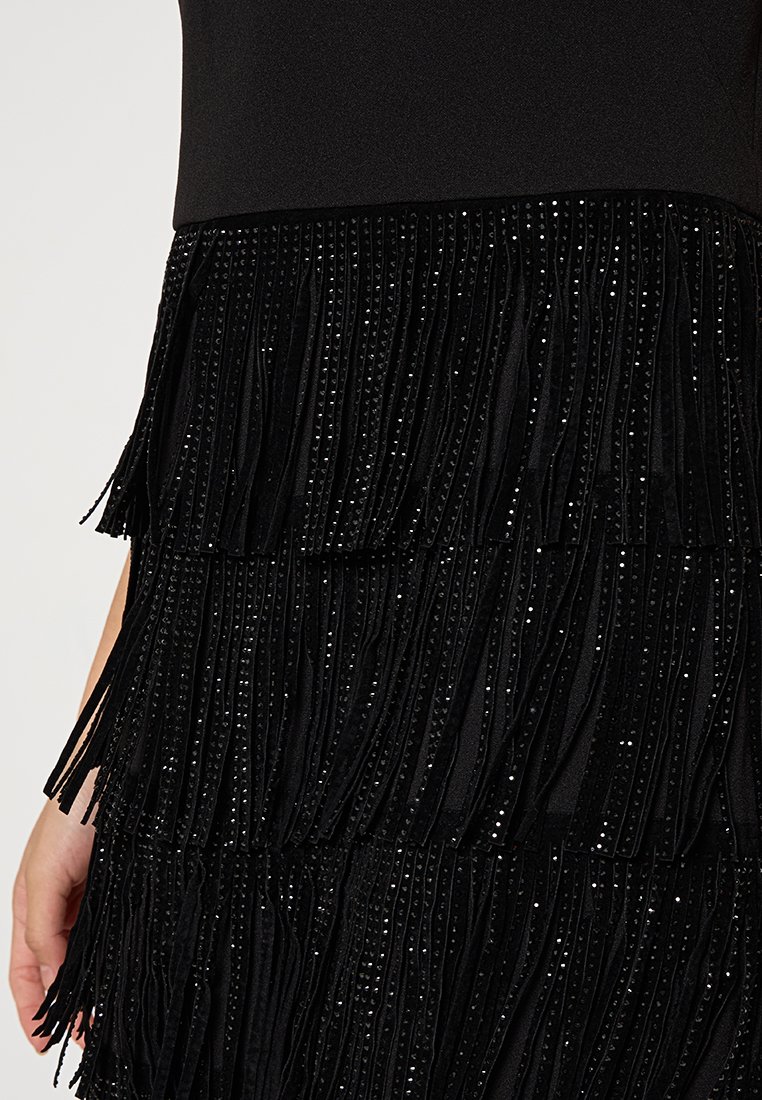 Czarna sukienka z dopasowanym górnym krojem i warstwową spódnicą z frędzlami. Spódnica ma błyszczące cekiny pomiędzy teksturowanym materiałem.