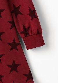 Czerwony, długi rękaw materiałowej bluzki z wyrazistym wzorem czarnych gwiazd, teksturowanym materiałem i marszczonymi mankietami dla dopasowanego wyglądu.