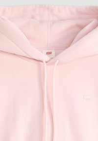 Svetlo ružová mikina vyrobená z mäkkej tkaniny, s kapucňou na šnúrku a malým bielym logom Levi's na hrudi. Jednoduchý dizajn bez vzorov.