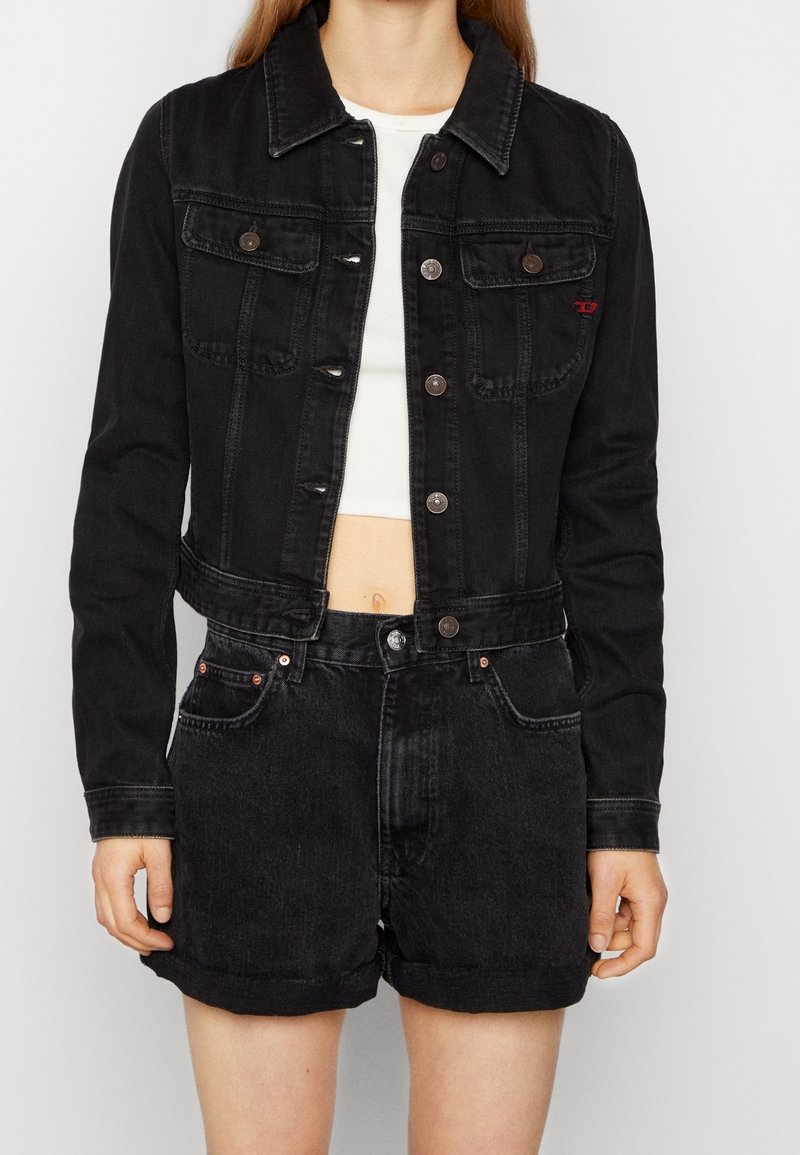 Kvinna som bär en kort svart denimjacka över en vit crop top, ihop med högmidjade svarta denimshorts.